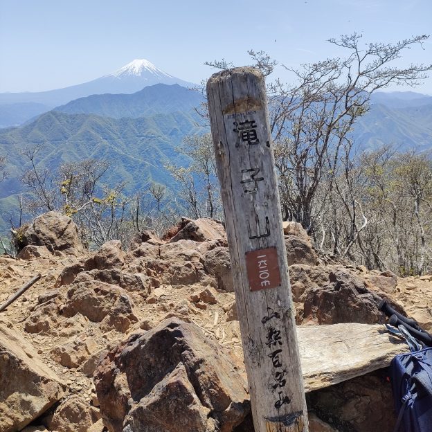 山頂の標識とその後ろに富士山が見える写真