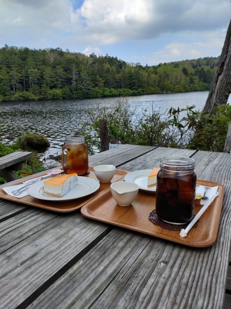 白駒池前のテーブルで杏ソースのチーズケーキとコーヒーを置いて記念写真